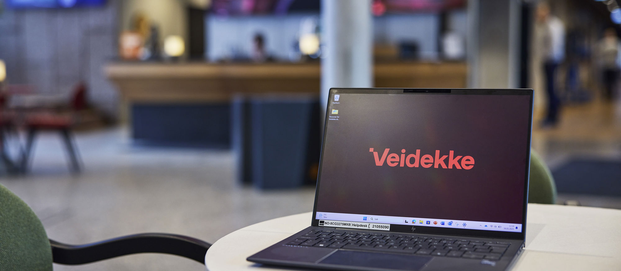 Laptop computer on a side table with a screen featuring the Veidekke logo