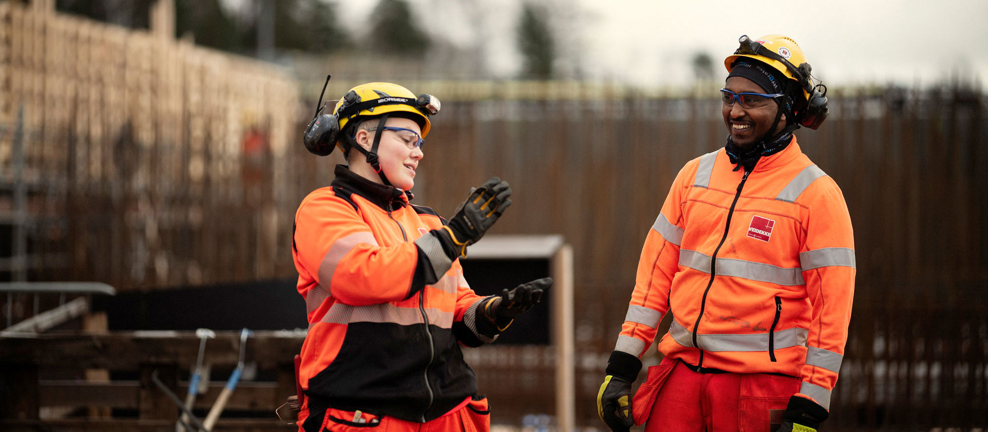 Man and woman chatting. Both wearing high-vis clothing. Photo.