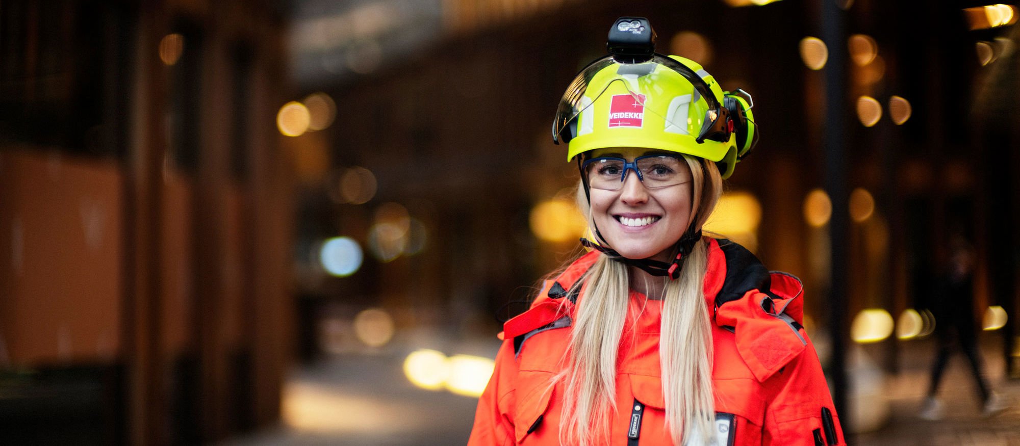 Woman with helmet and high-vis clothing smiling at camera. Photo.